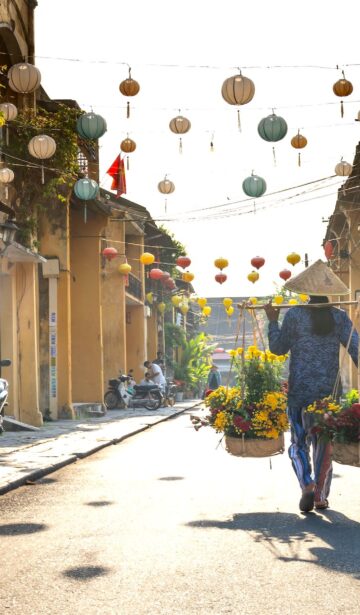 unrecognizable ethnic woman with baskets of flowers strolling on street in vietnam