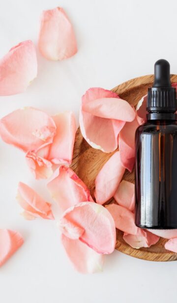 composition of cosmetic bottle with pink rose petals and wooden plate