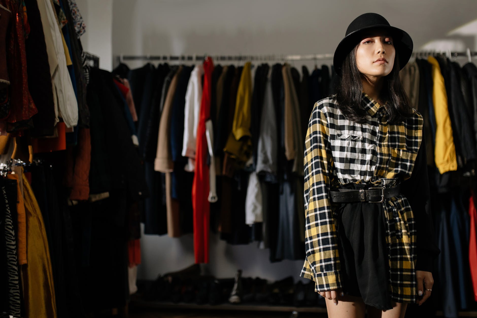 a woman wearing plaid long sleeves shirt and black skirt standing near clothes rack while looking at the camera